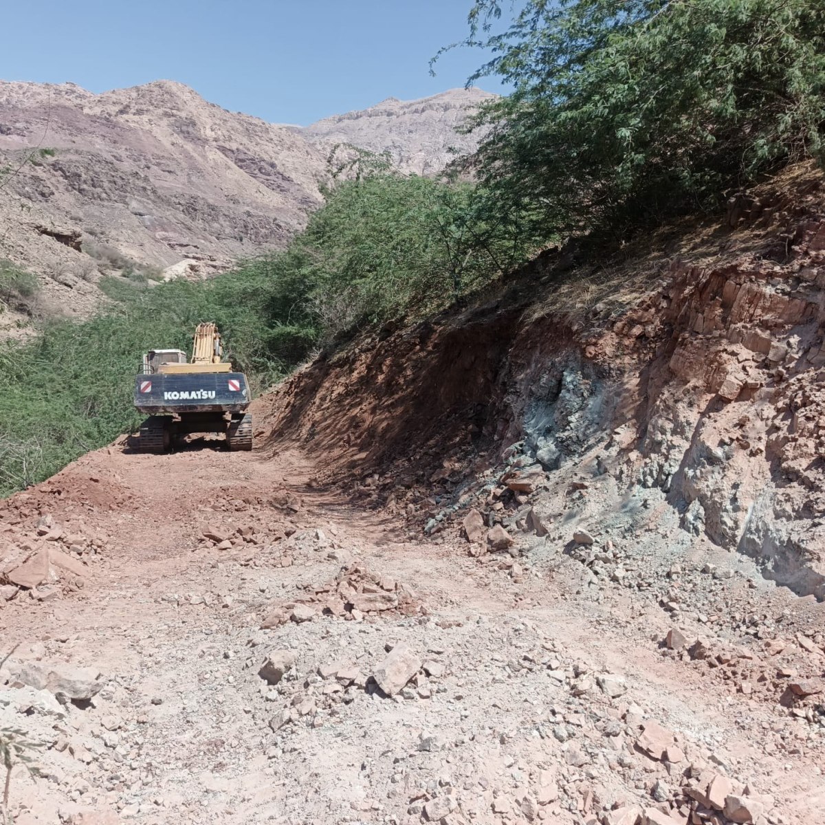 Excavator on a newly constructed access road beside exposed rock at the Ghor Fifa exploration site.