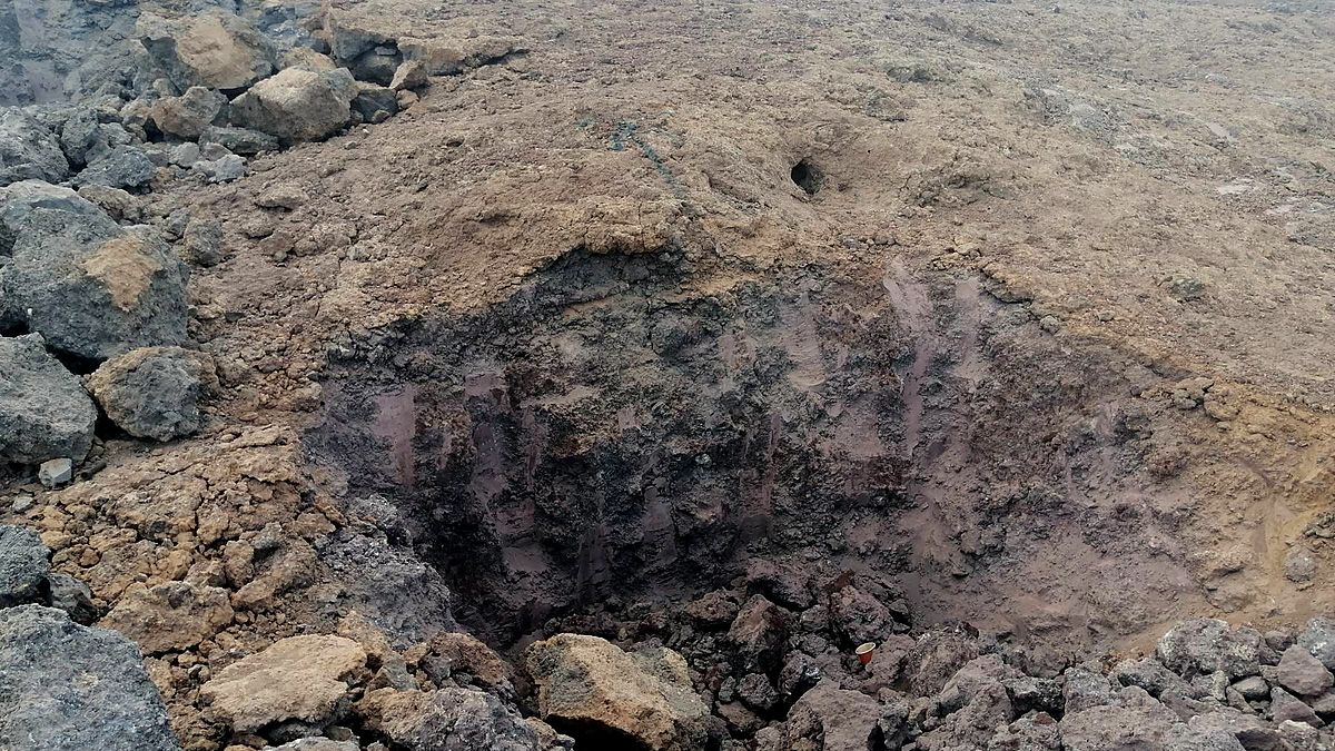 Exploration pit in the Ung Ar Rustom volcanic field, with dark basalt blocks around it