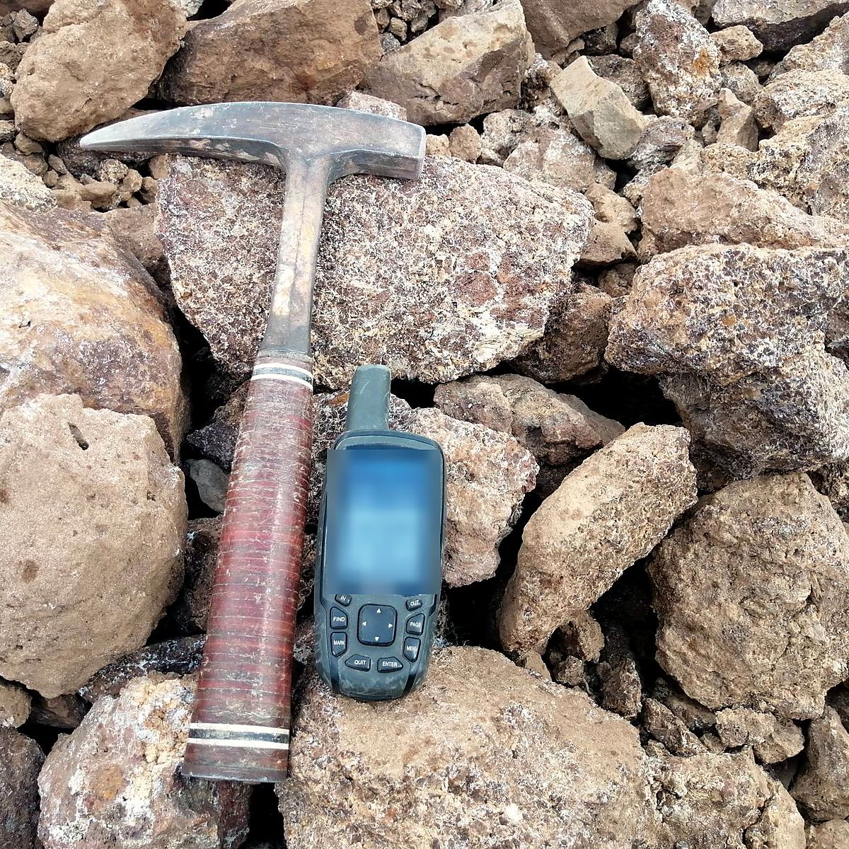 Volcanic tuff blocks at a sampling point, with a geological hammer and handheld GPS for scale
