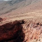Exploration trench cut into reddish zeolitic tuff, with volcanic hills behind, at Ung Ar Rustom in northeastern Jordan