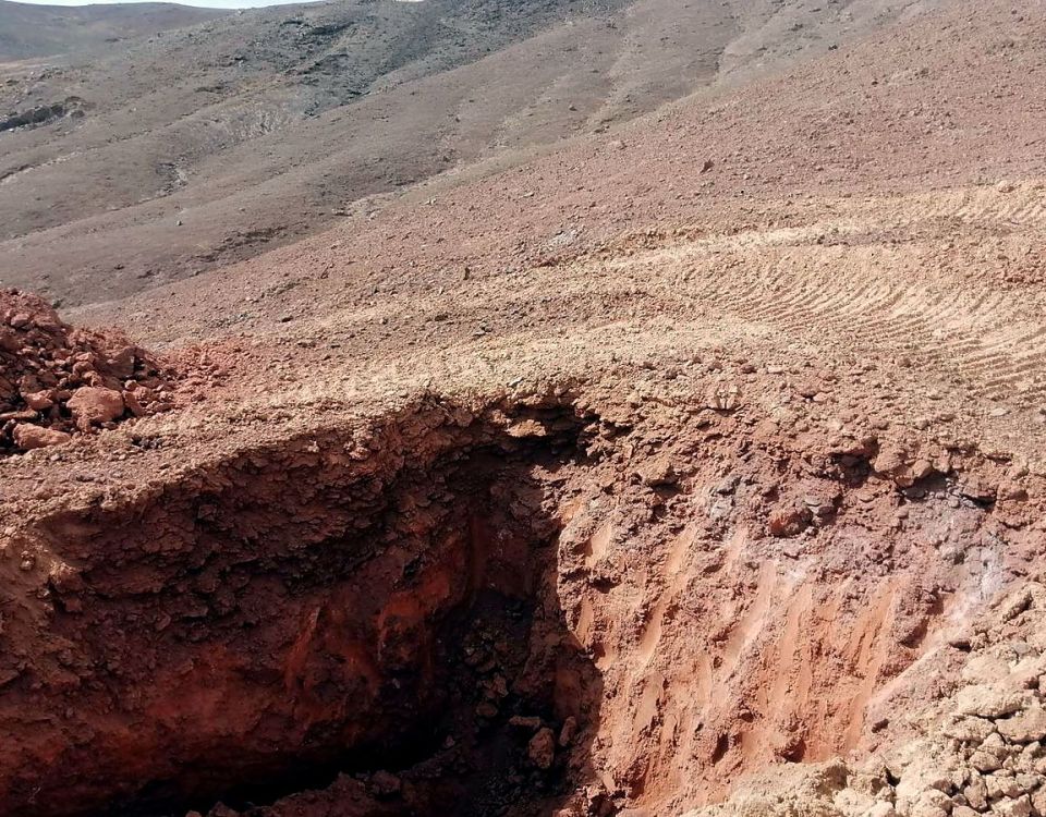 Exploration trench cut into reddish zeolitic tuff, with volcanic hills behind, at Ung Ar Rustom in northeastern Jordan